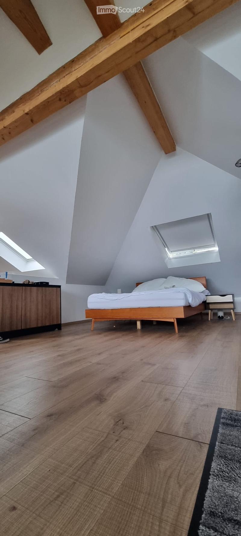 Modern attic bedroom with wooden floors, slanted ceilings, skylights, a bed, nightstand, and a cabinet.