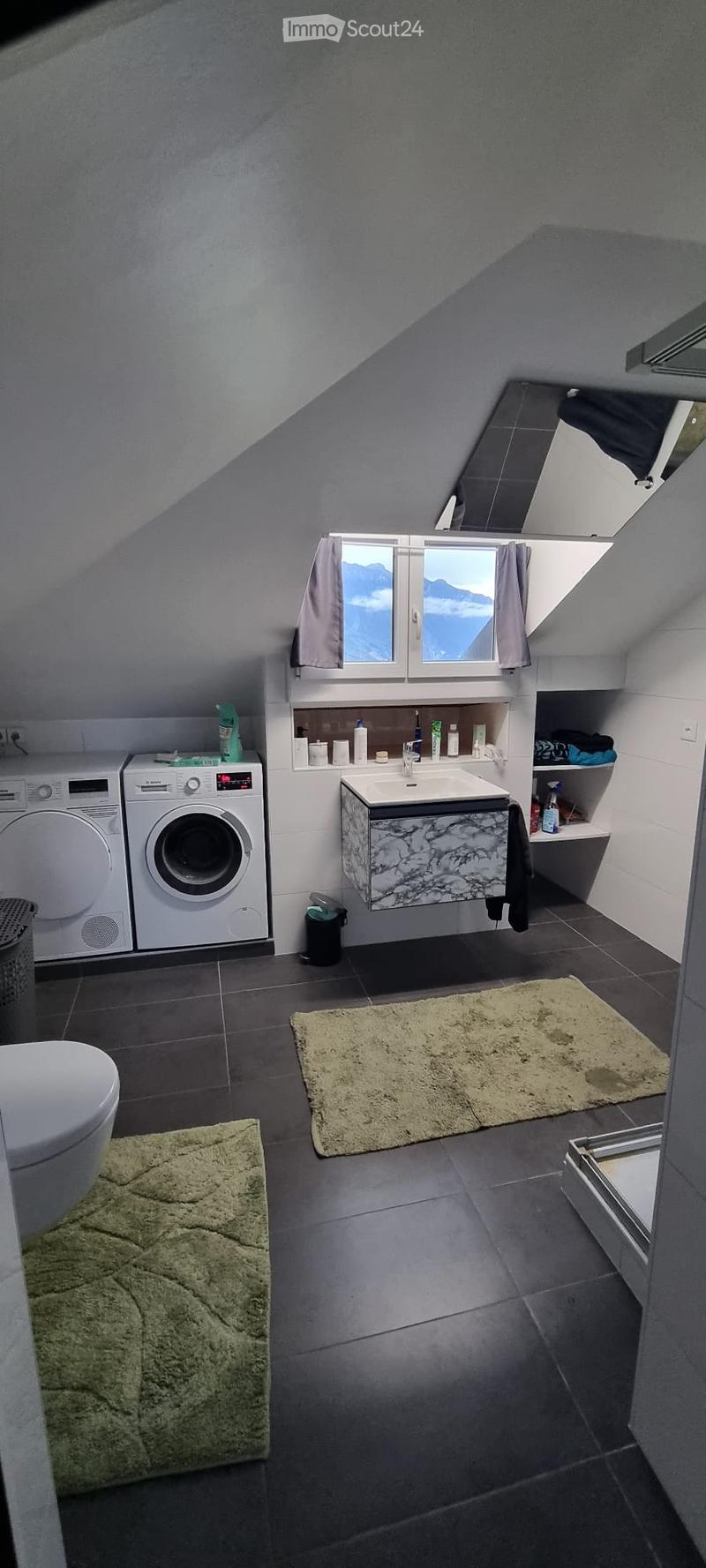 Modern bathroom with dark tiled floor, white toilet, marble sink, two washing machines, and a window with mountain view.
