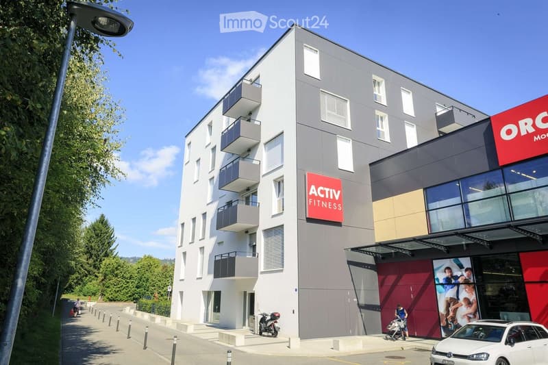 Modern multi-story building with grey and white facade, balconies, and commercial signage for 'ACTIV FITNESS' and 'ORC'.