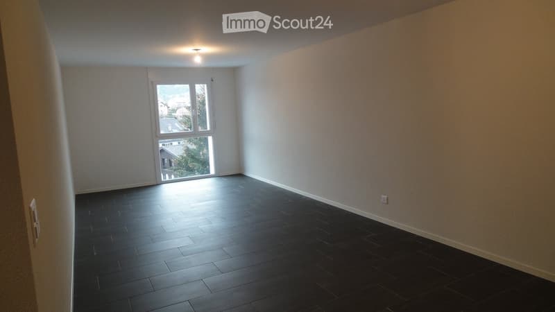 Empty room with dark tiled floor, white walls, and large window letting in natural light.