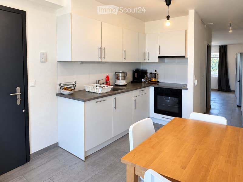 Modern kitchen with white cabinets, a wooden dining table, and various appliances including an oven, refrigerator, and coffee maker.