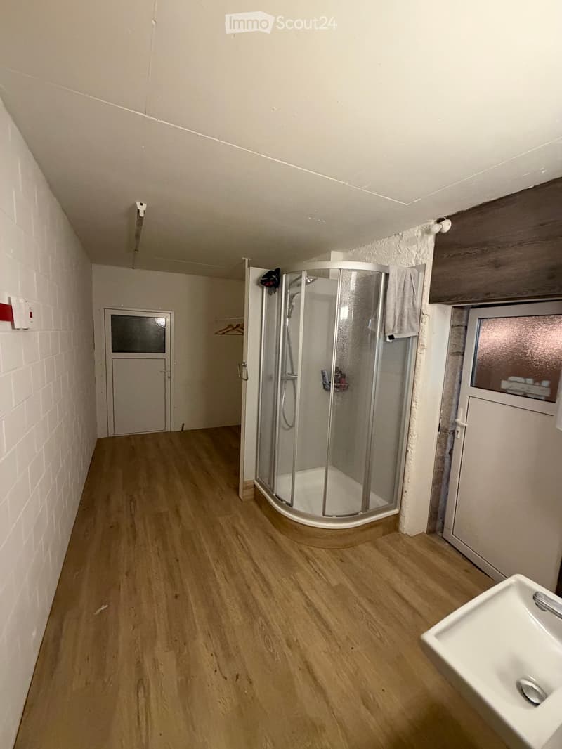 Bathroom with wooden flooring, white brick walls, a white sink, and a glass-enclosed shower stall.