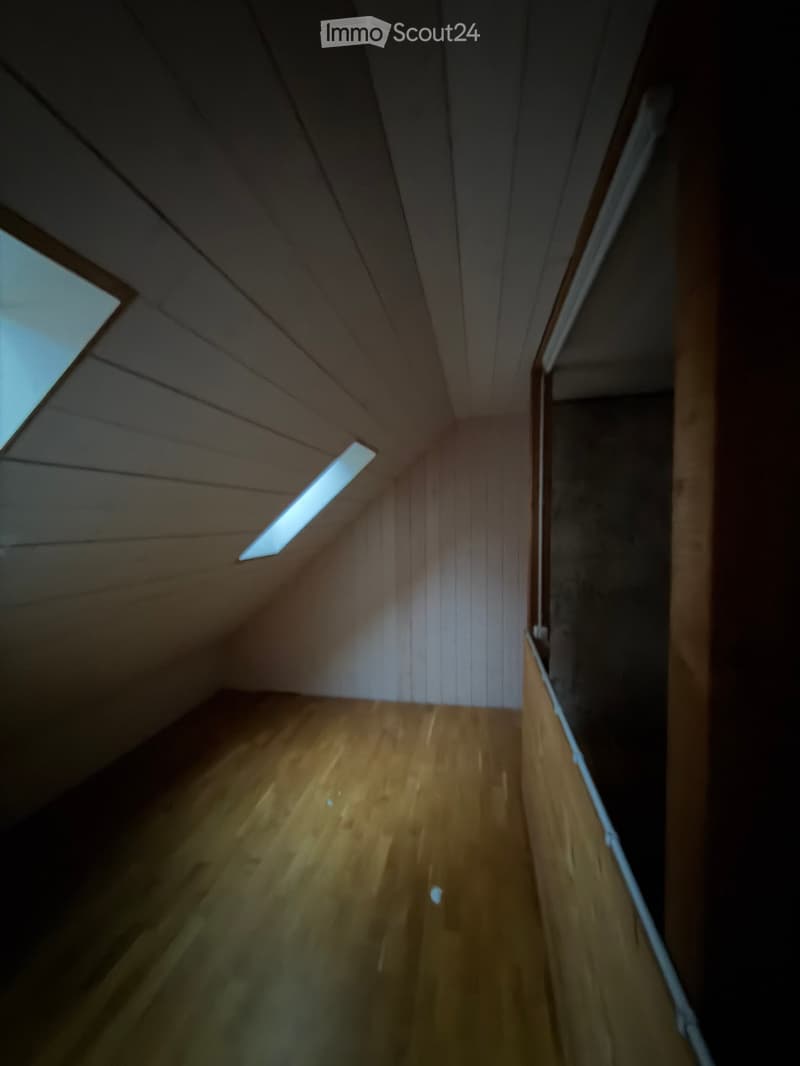 A narrow wooden hallway with slanted wooden ceiling and small skylight windows, leading to an open area.