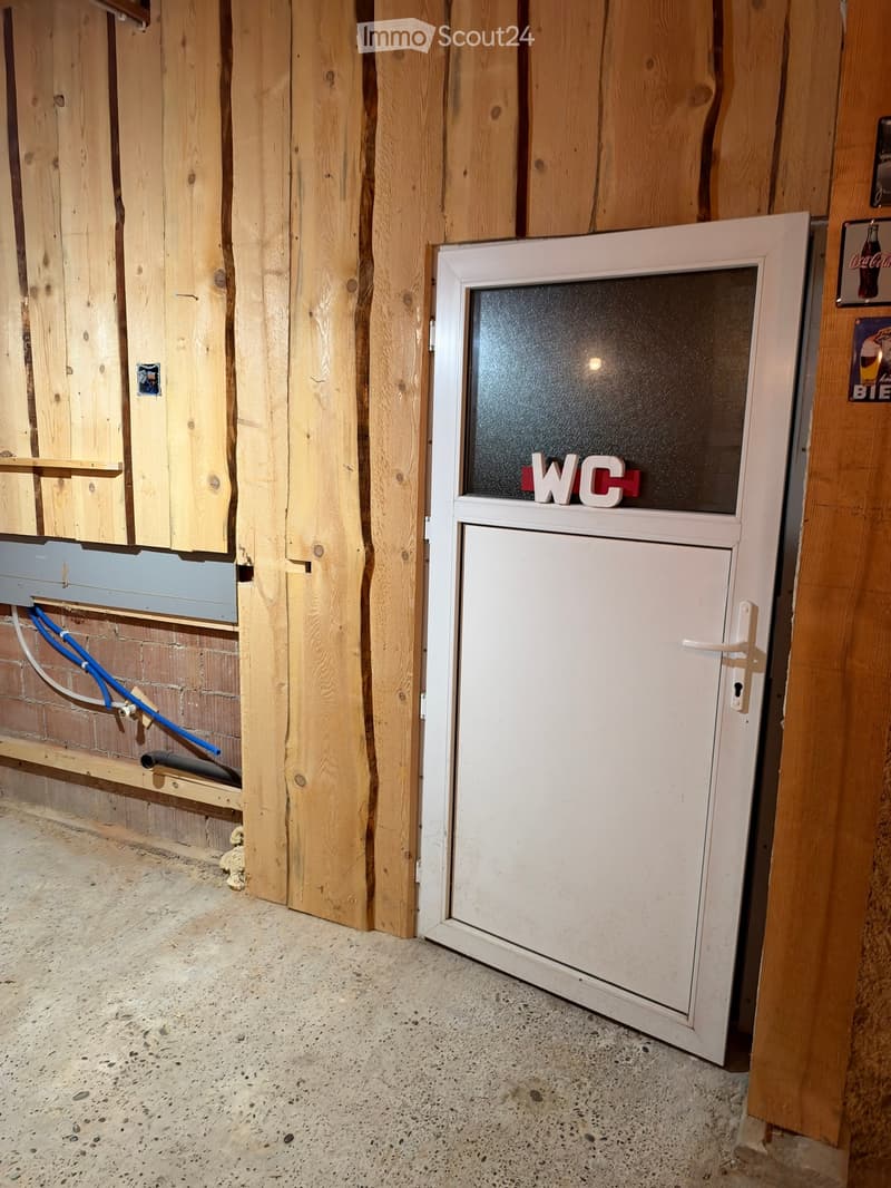 Empty room with wooden walls, concrete floor, and a white door labeled "WC" with a frosted glass panel.