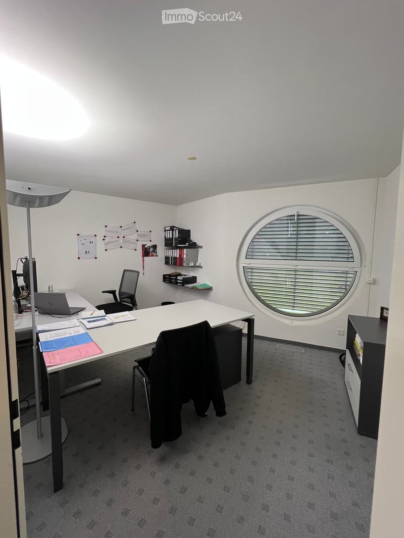 Office space with a large desk, chairs, laptop, floor lamp, shelves with books and files, and papers on the desk.
