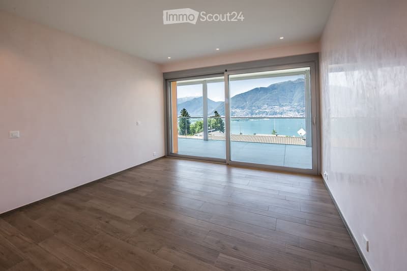 Empty room with wooden flooring, large sliding glass doors leading to a balcony with a scenic mountain and lake view.
