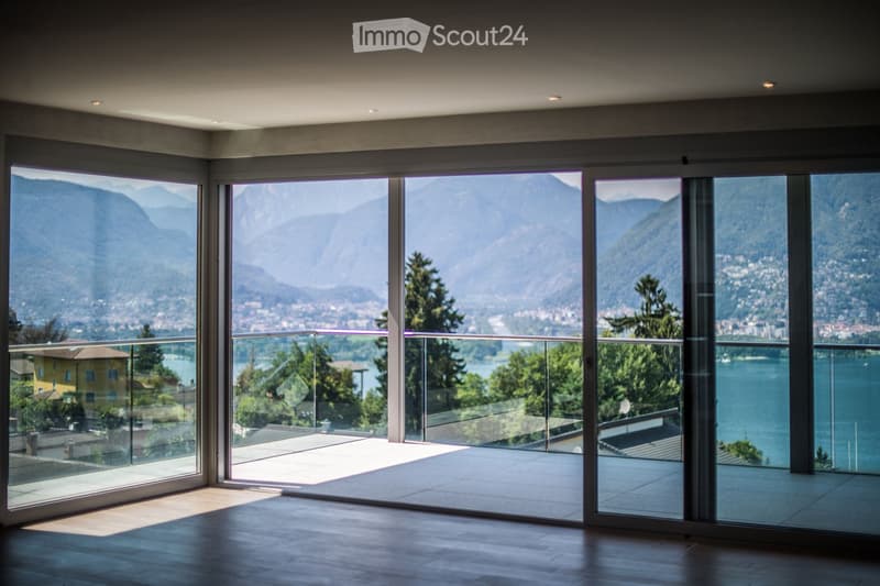 Empty room with large glass sliding doors opening to a balcony, overlooking a scenic lake and mountain view.