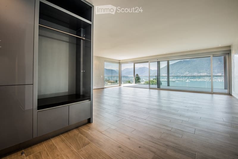 Spacious, unfurnished room with wooden flooring, large glass windows offering a scenic mountain and lake view, and built-in closet with dark wood finish.