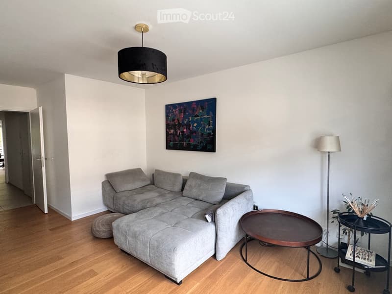 Modern living room with grey sectional sofa, wooden coffee table, floor lamp, side table, and artwork on the wall.