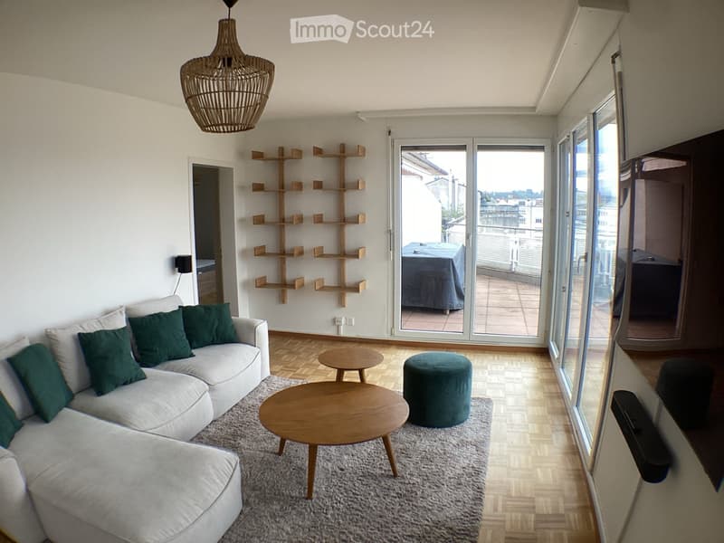Modern living room with a white sectional sofa, green cushions, wooden coffee table, small round table, green ottoman, and a large sliding glass door leading to a balcony.