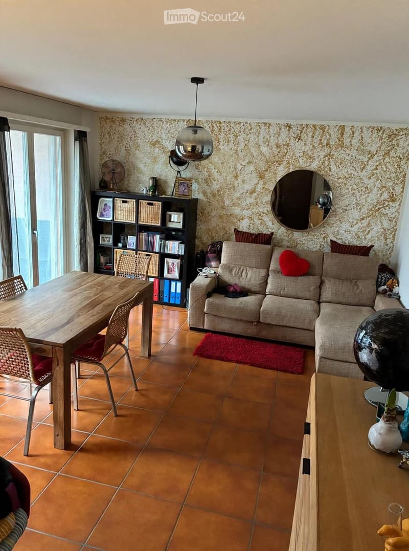 Living room with a beige sofa, wooden coffee table, dining table with chairs, bookshelf, mirror, fan, globe, and decorative items.