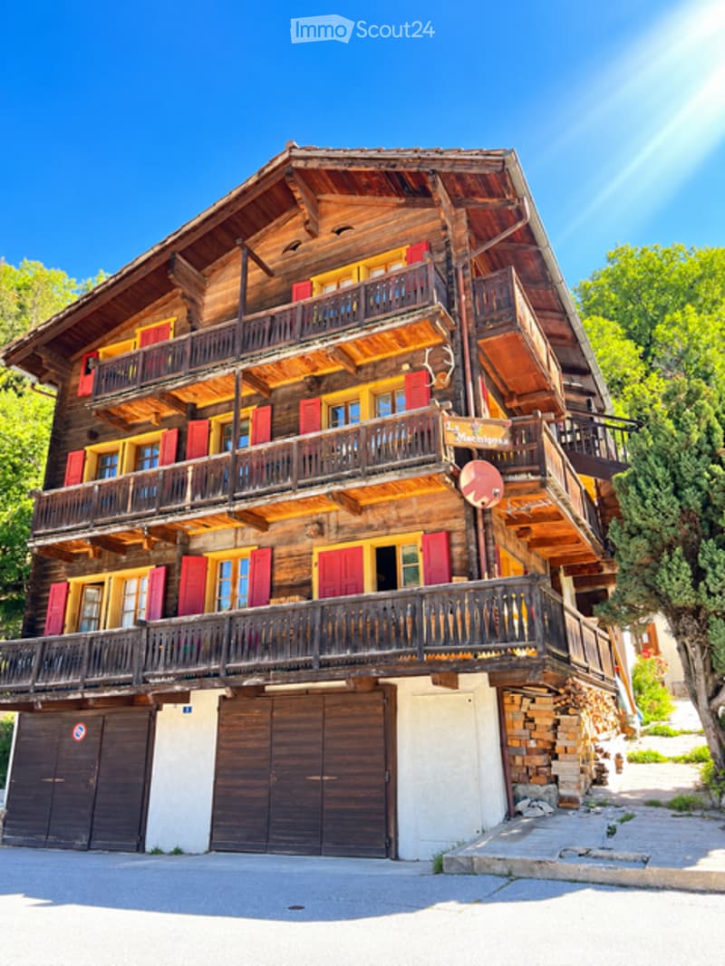 A large, multi-story wooden chalet with red shutters, balconies, and a garage.
