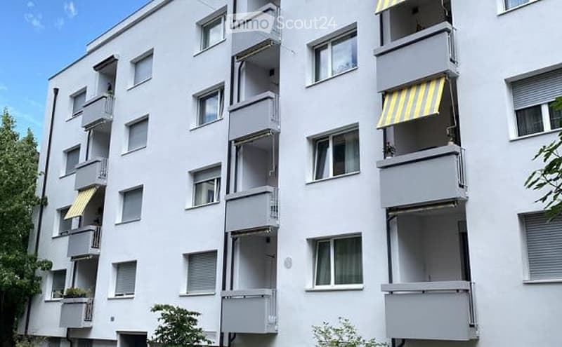 Multi-story residential building with multiple balconies and windows, featuring yellow striped awnings on some balconies.