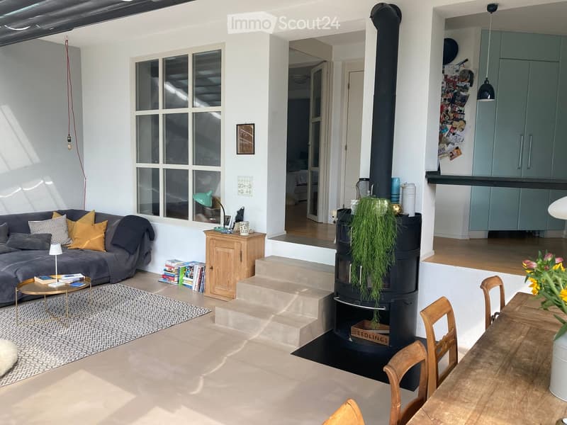 Open-plan living and dining area with a grey sofa, wooden dining table, fireplace, and modern decor.