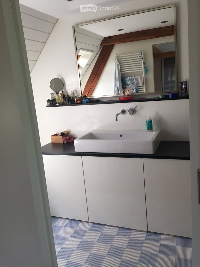 Modern bathroom with a white sink, large mirror, towel rack, and various toiletries on the counter.