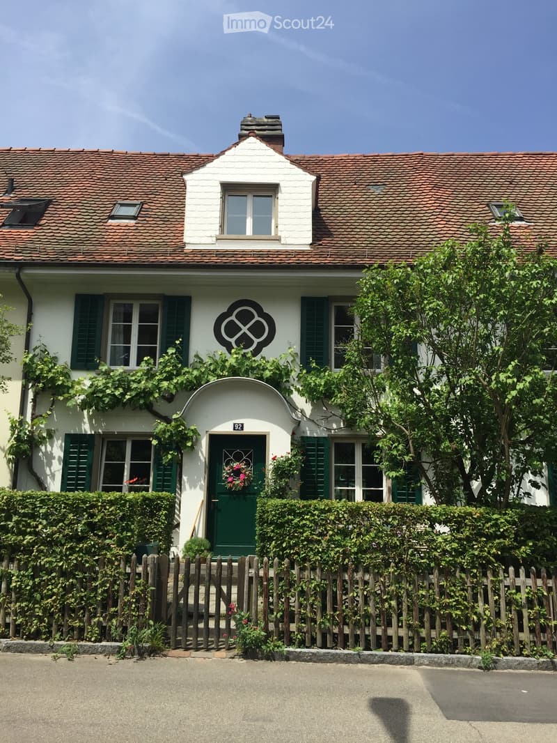 Two-story house with white walls, green shutters, red-tiled roof, and a decorative entrance featuring a wreath on the door.