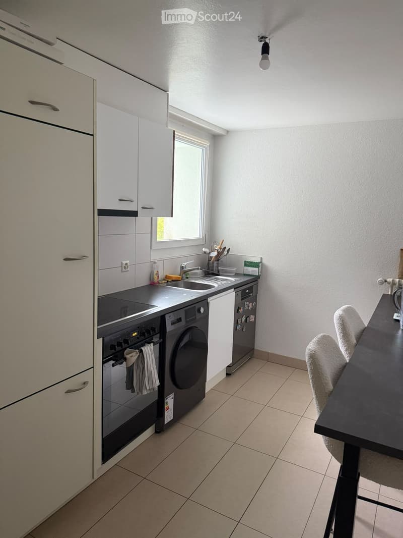 Modern kitchen with white cabinets, stainless steel appliances, a sink, and a small dining area with a table and chairs.