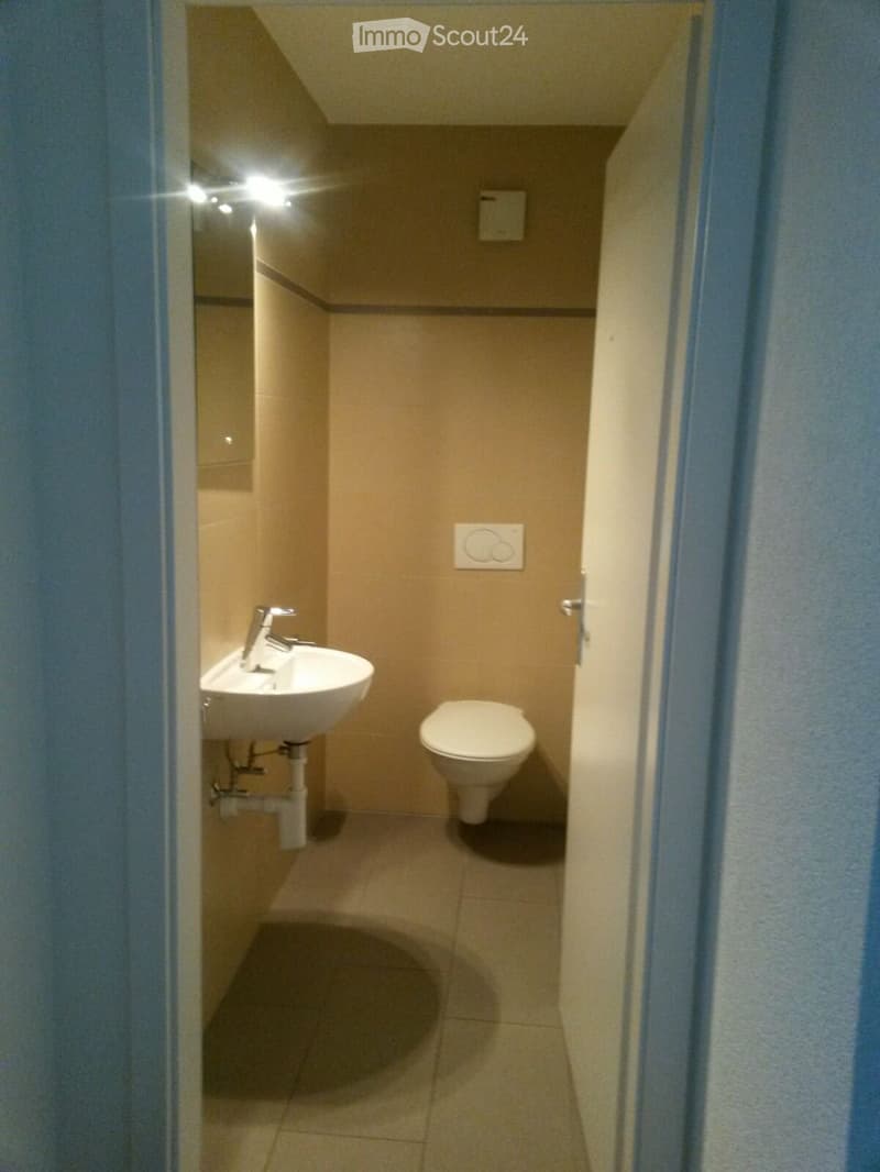 Small bathroom with beige tiled walls and floor, featuring a white sink with a chrome faucet and a white toilet.