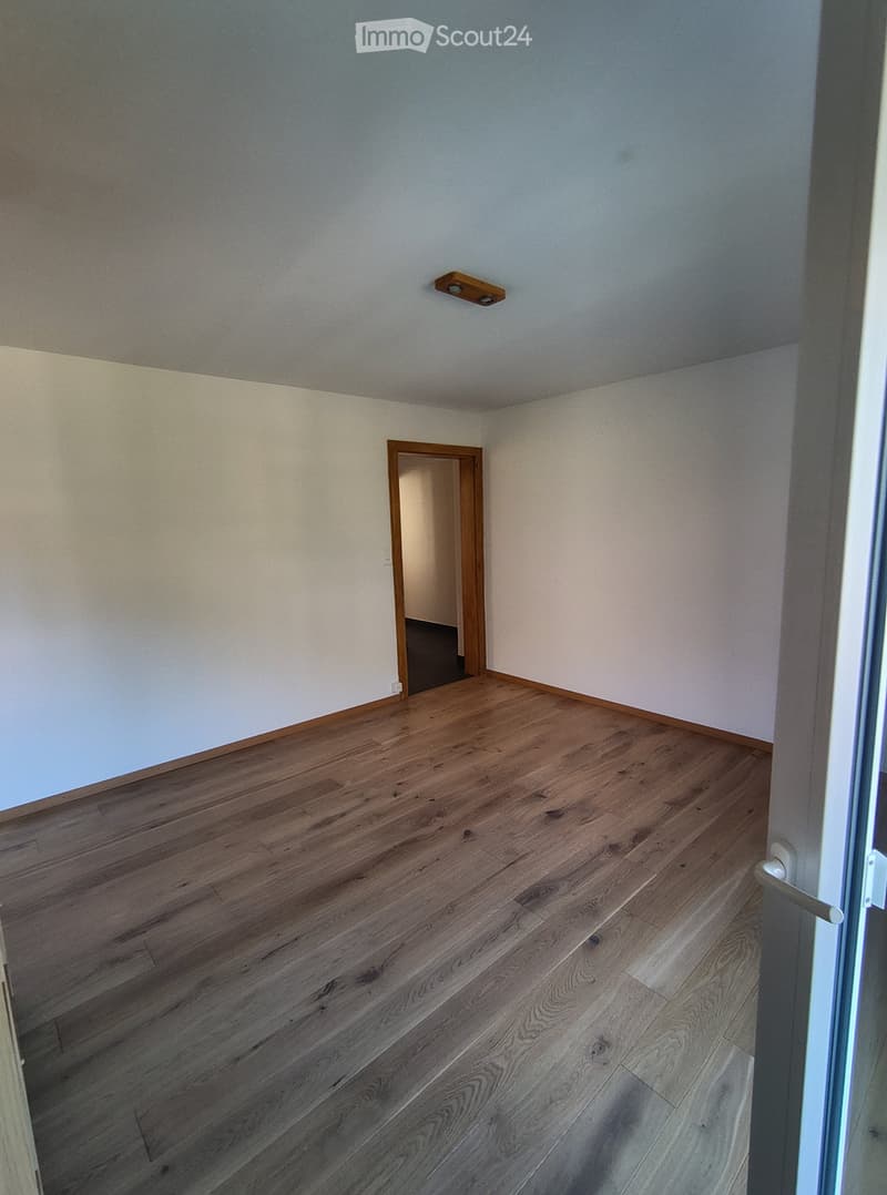 Empty room with wooden flooring and white walls, featuring a single door leading to another space.