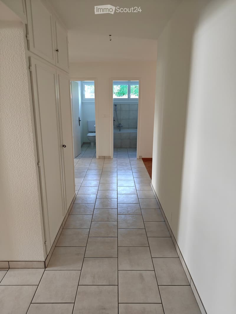 Empty hallway with tiled floor, white walls, and two open doors leading to bathrooms with visible fixtures.