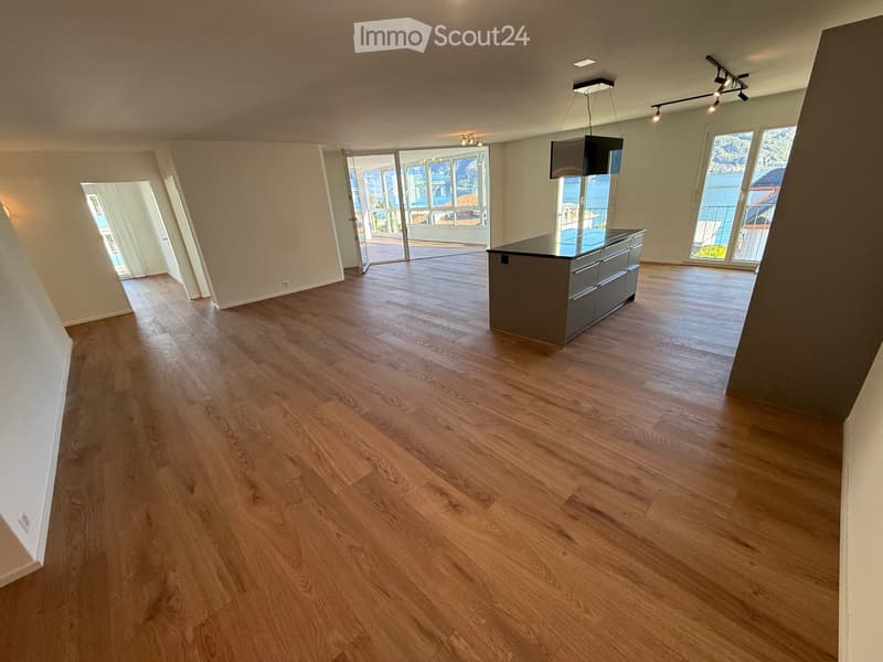 Open-plan space with wooden flooring, a kitchen island, large windows, and sliding glass doors leading to a balcony.