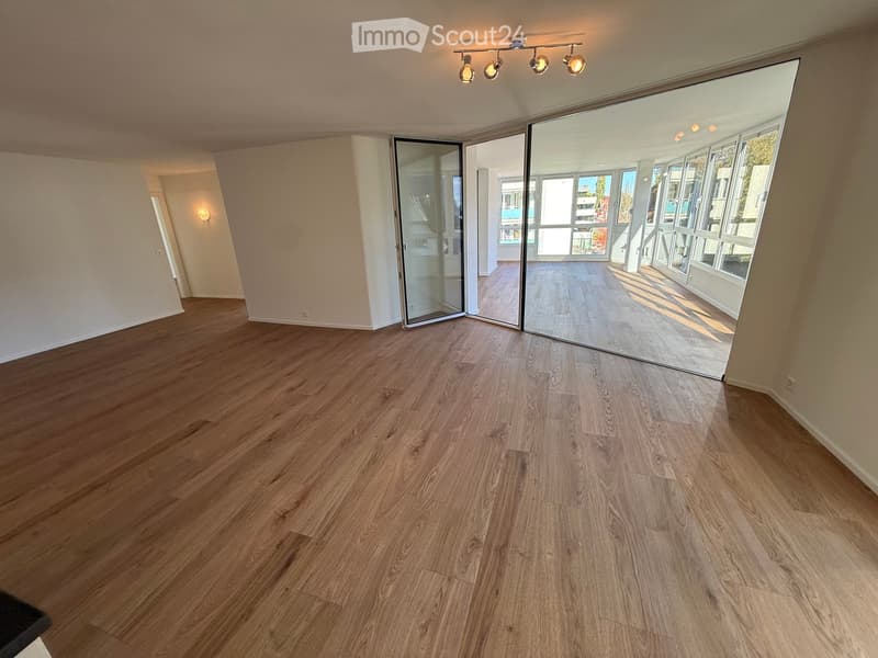 Empty room with wooden flooring, large sliding glass doors leading to a balcony, and recessed lighting.