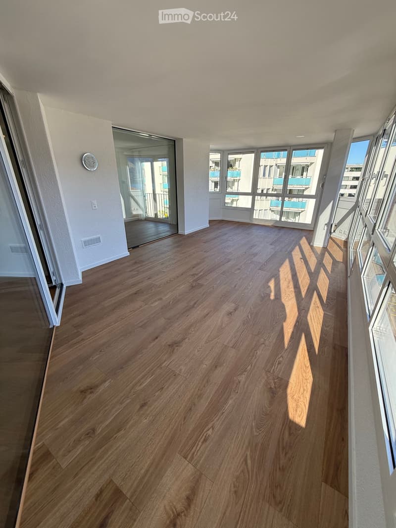 Empty room with wooden flooring, large windows, and sliding glass doors leading to a balcony.