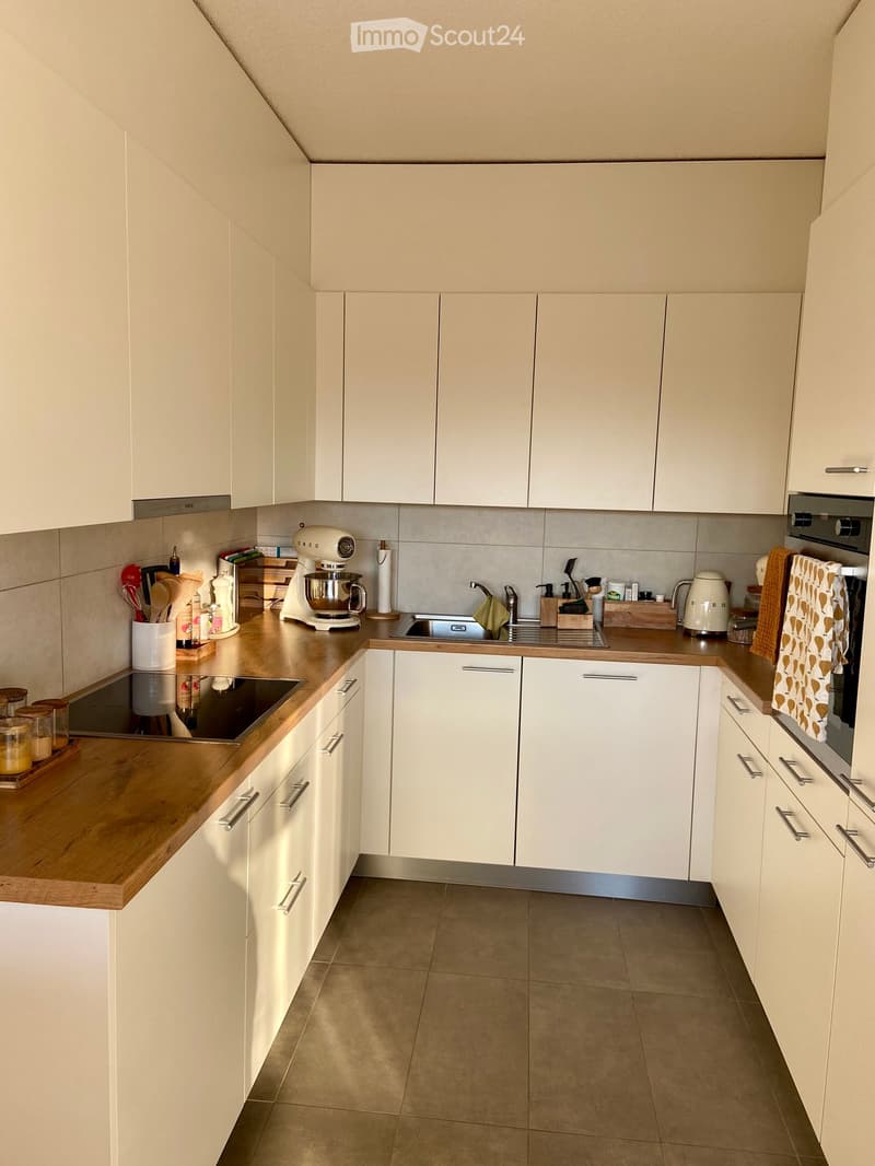Modern kitchen with white cabinets, wooden countertops, and stainless steel appliances. Includes a mixer, oven, sink, and various kitchen utensils.