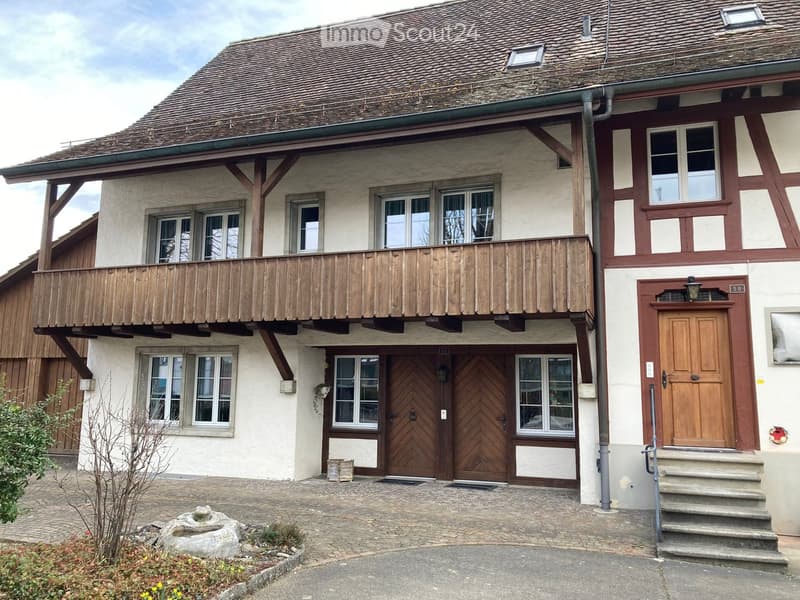 Two-story traditional house with a wooden balcony, multiple windows, and a tiled roof.