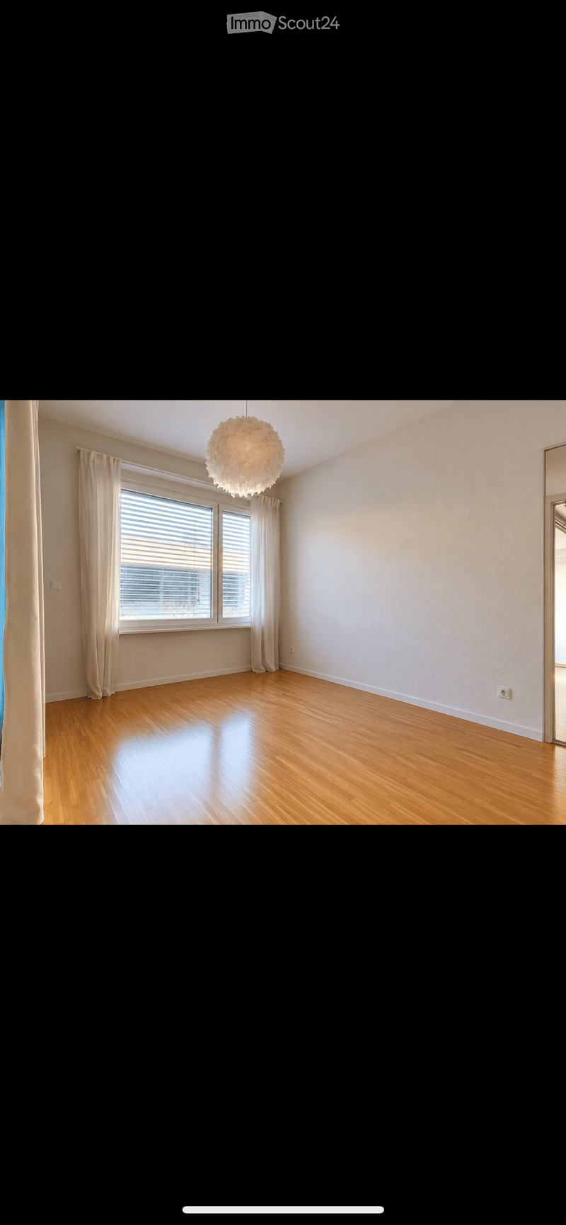 Empty room with wooden flooring, large window with blinds, and a hanging light fixture.