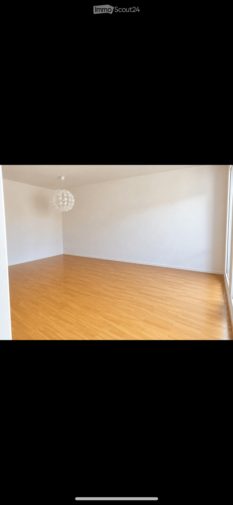 Empty room with light-colored walls and wooden flooring, featuring a single modern chandelier light fixture.