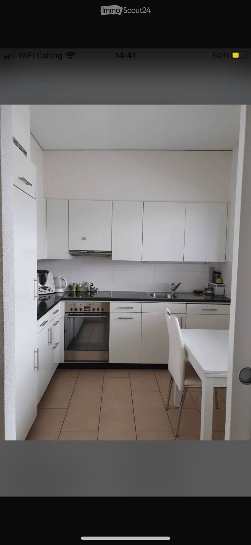 Modern kitchen with white cabinets, stainless steel appliances, and a small dining area with a white table and chair.