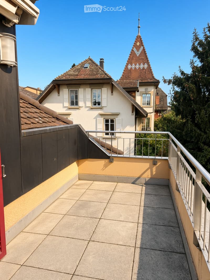 Balcony with tiled floor, metal railing, and view of neighboring houses with distinctive rooflines.