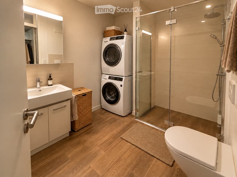Modern bathroom with a white sink, mirror, toilet, glass-enclosed shower, and stacked washer/dryer unit. Features a wicker basket, towel, and a small rug on the wooden floor.