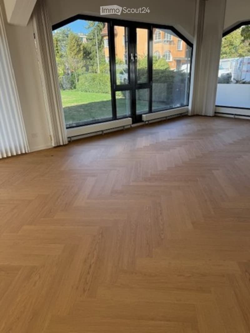 Empty room with wooden flooring, large windows, and white walls. No furniture or equipment present.