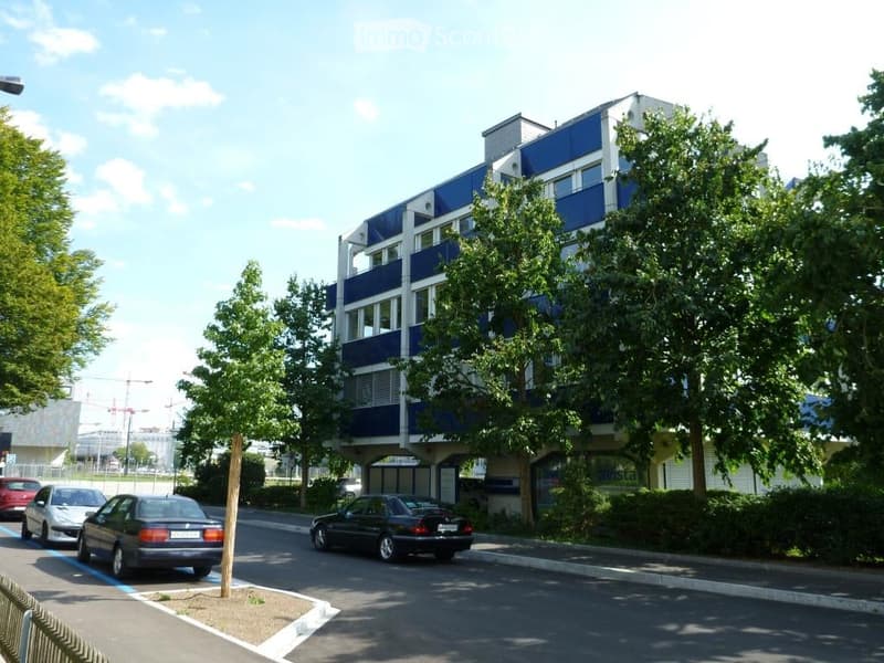 4-story building with blue walls, white windows, cars parked on the side, trees, street light, parking lot, balcony