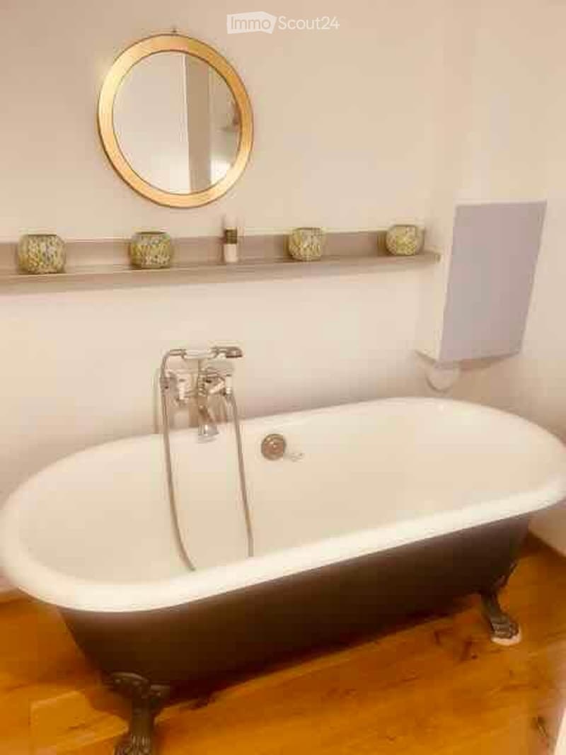 Bathroom with a classic clawfoot bathtub, a round gold-framed mirror, and a shelf with decorative items above the tub.