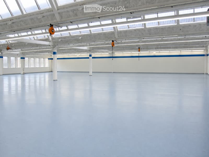 Large, empty industrial-style room with white walls, polished blue floor, and exposed white structural beams and lighting. No furniture or equipment present.