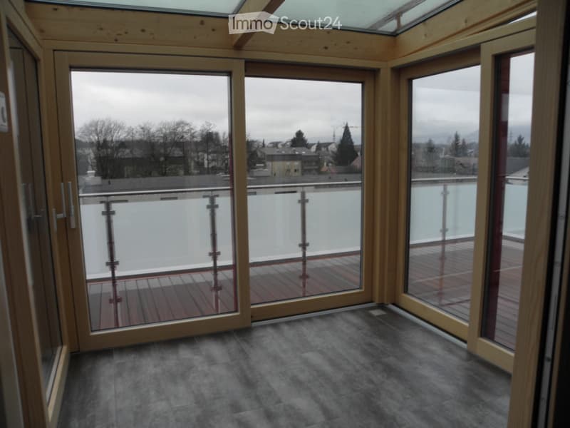 Empty room with large glass doors leading to a balcony or terrace, wooden flooring, and a view of the surrounding area.