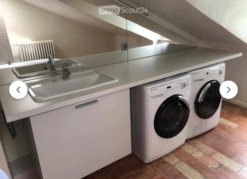 Modern bathroom with a double sink, faucet, and a built-in washing machine and dryer unit.