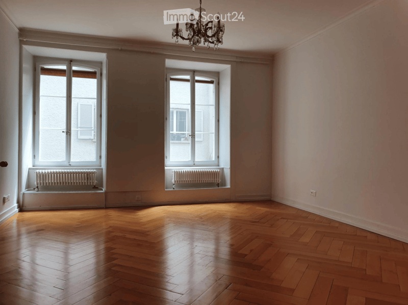 Empty room with wooden flooring, large windows, radiators, and a chandelier.