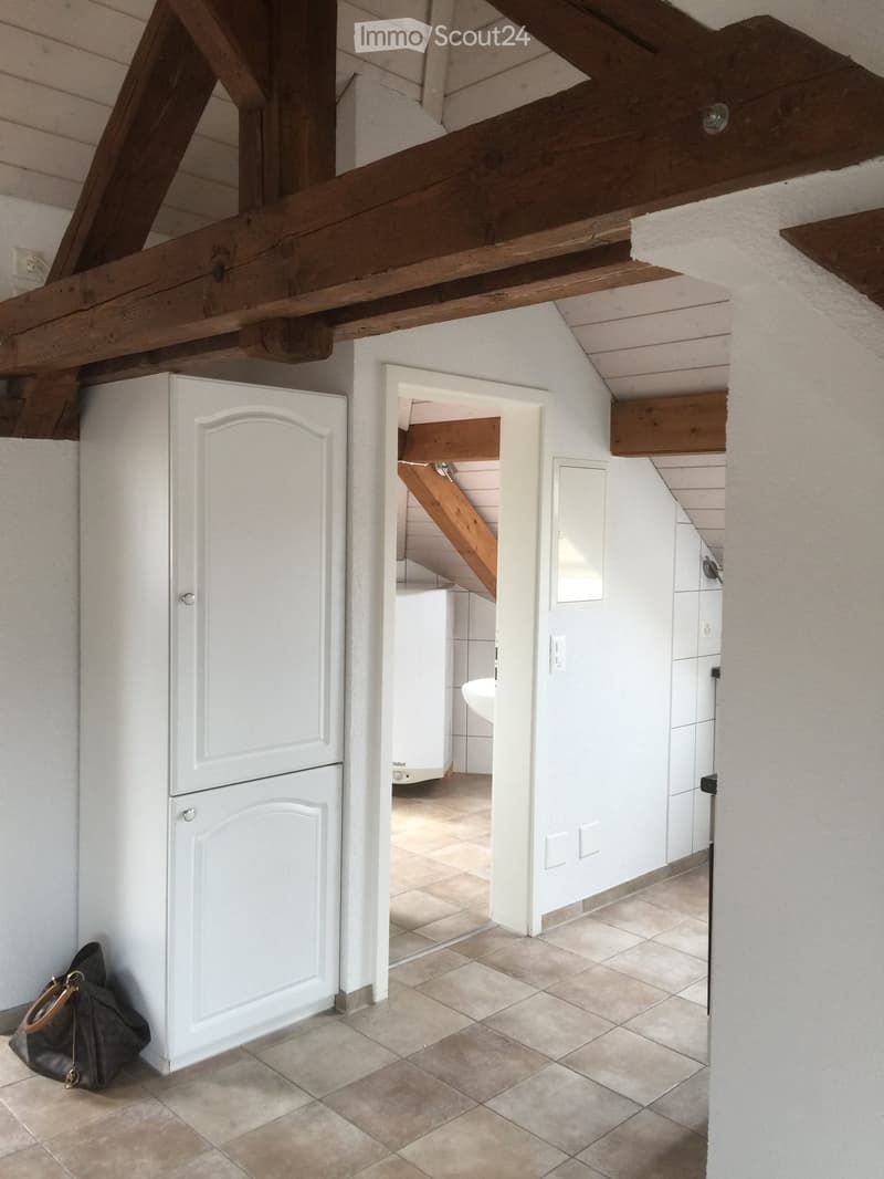 Hallway with exposed wooden beams, tiled floor, white walls, and a partially visible bathroom with a sink and white cabinets.