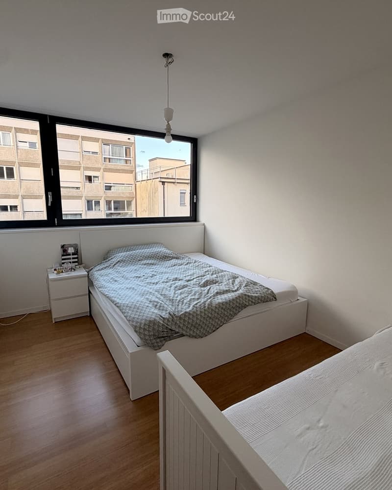 Cozy bedroom with two single beds, a nightstand, and a large window overlooking a building.