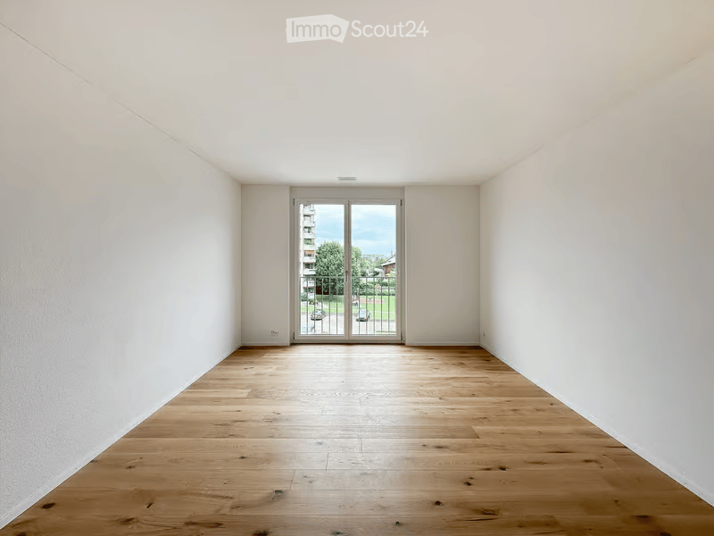 Empty room with light wooden flooring and white walls, featuring a large glass door leading to an outdoor area.