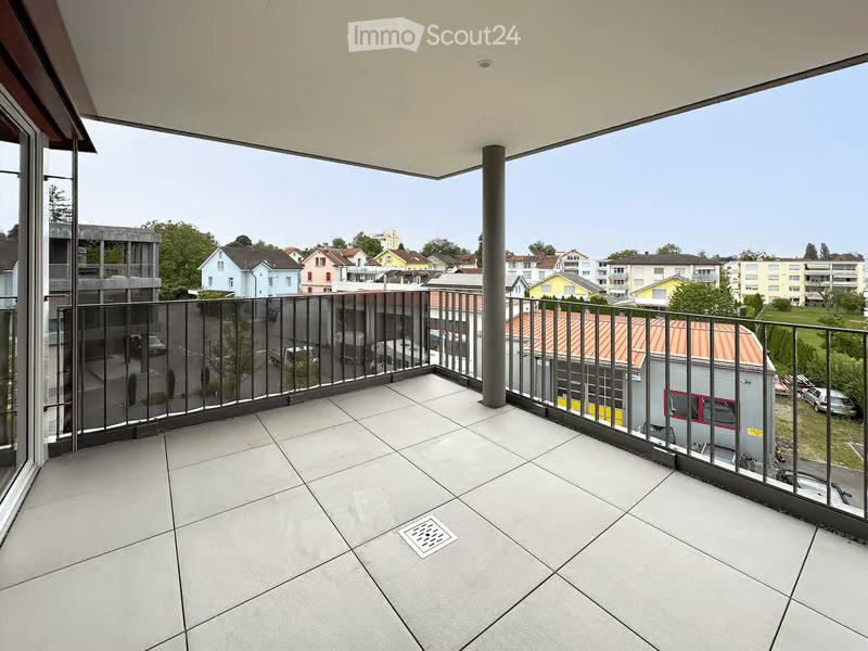 Spacious balcony with modern tiled flooring, black metal railing, and a view of the surrounding residential area.