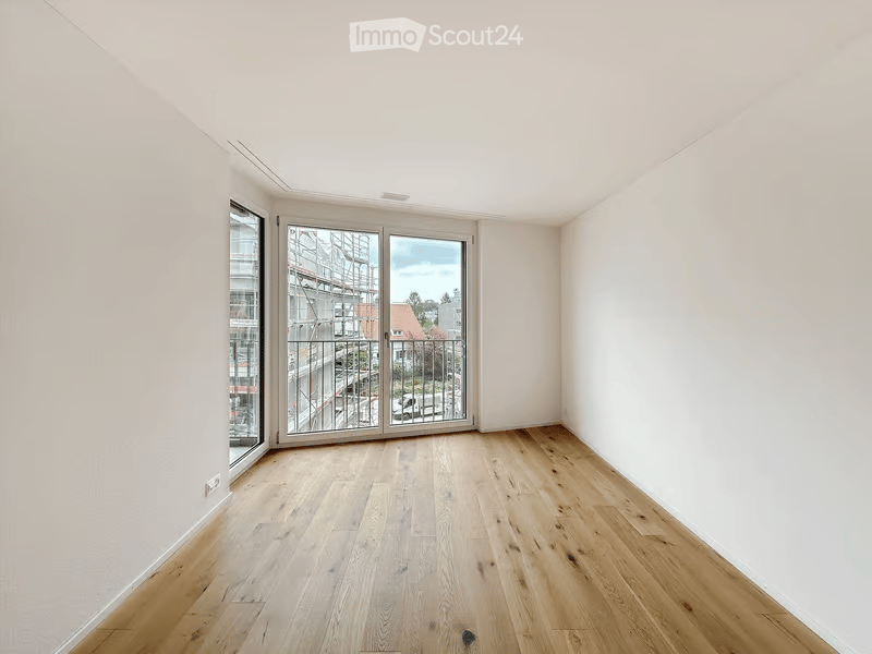 Empty room with wooden flooring, white walls, large windows, and a sliding glass door leading to a balcony.