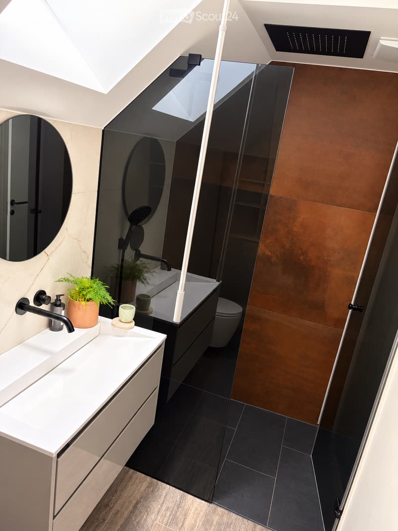 Modern bathroom with white sink, black faucet, round mirror, toilet, and small plant on counter.
