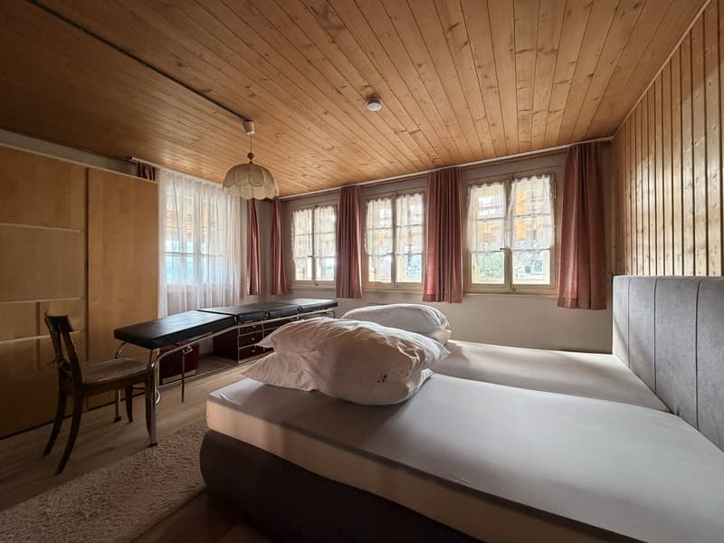 Bedroom with wooden ceiling, two beds, wooden chair, desk, wooden wardrobe, white curtains, white pillows, white rug