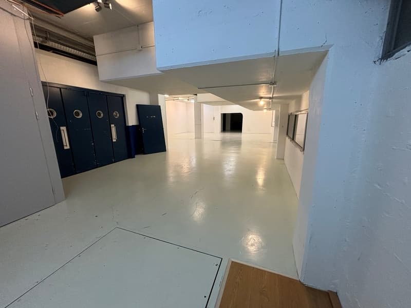 wide room with white flooring, white walls, blue storage units, open area at the end