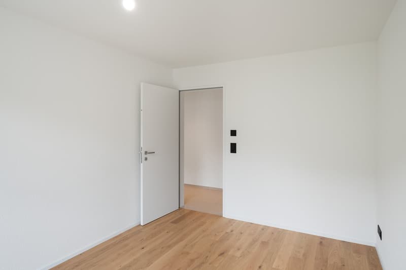 Empty room with white walls, hardwood flooring, and a white door.